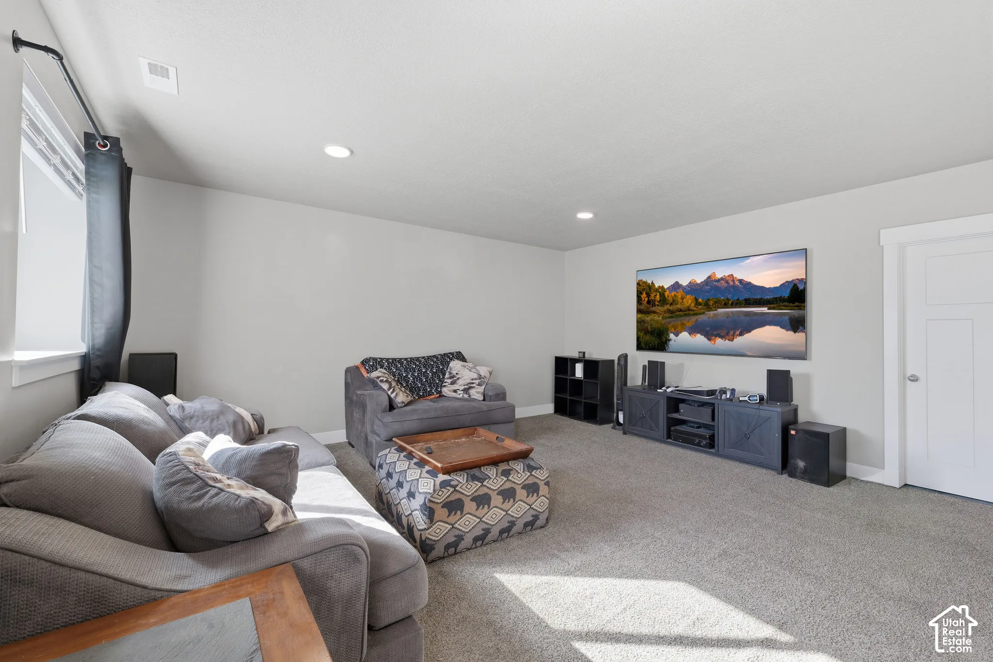 Neutral-toned living space featuring wall-to-wall carpeting, recessed ceiling lighting, and a multi-panel interior door with wide trim