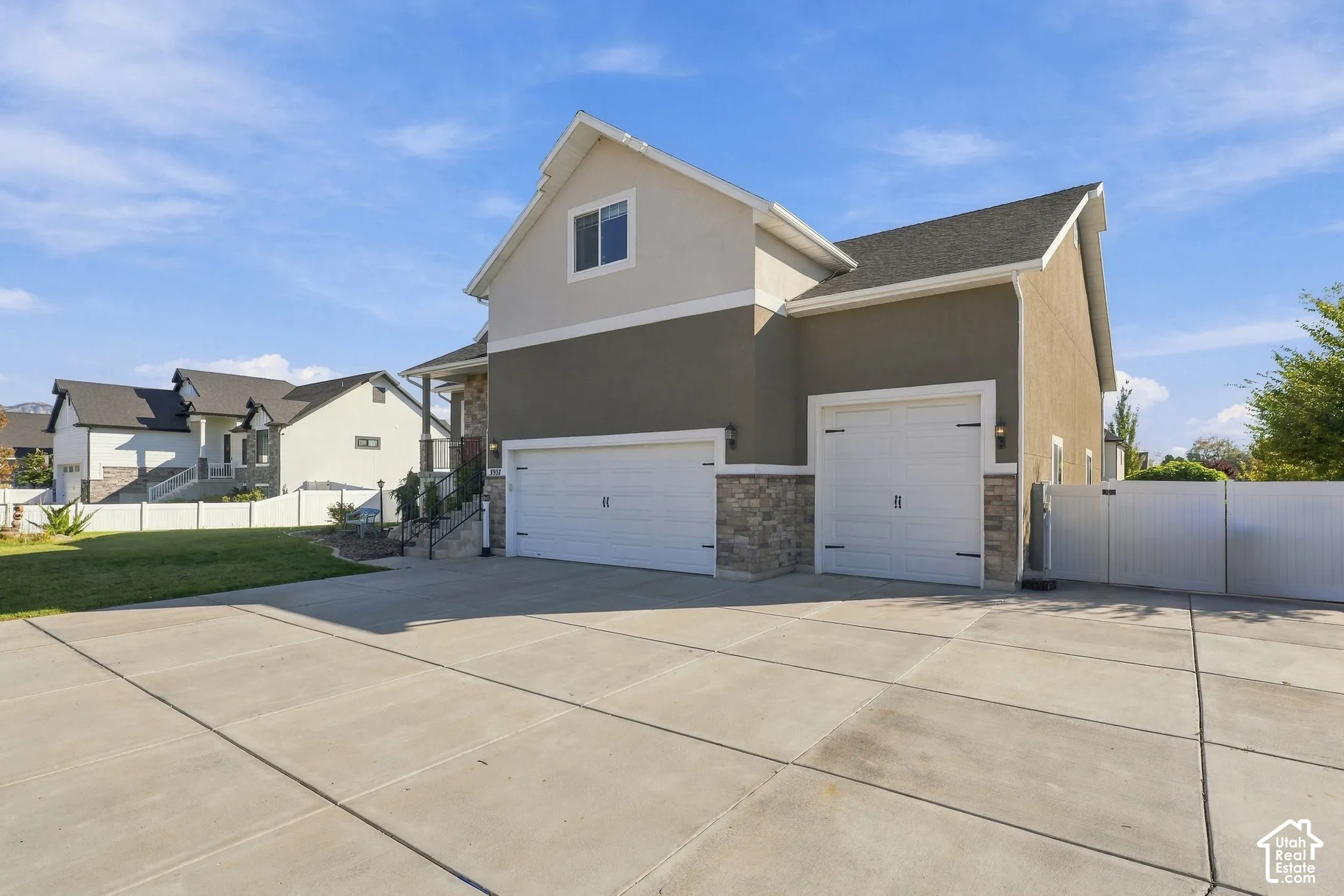 Multi-level exterior featuring a combination of stucco and stone veneer siding, an attached three-car garage, and a spacious concrete driveway