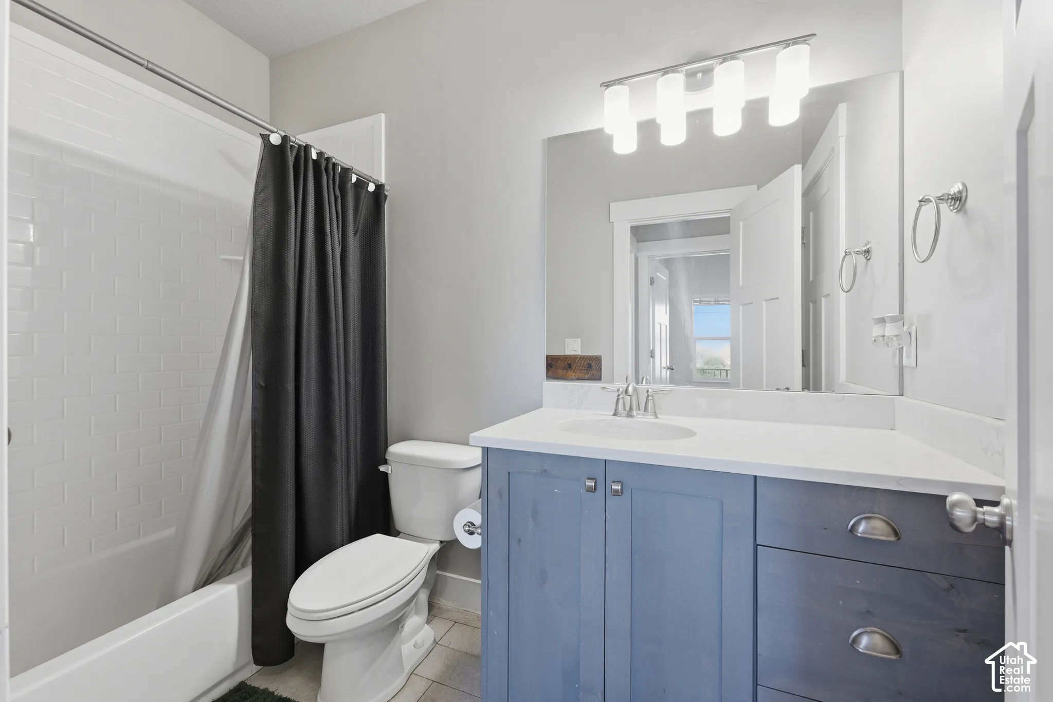 Bathroom featuring a custom blue-finish vanity with a white countertop, subway tile shower surround, four-bulb vanity lighting, and large wall-mounted mirror