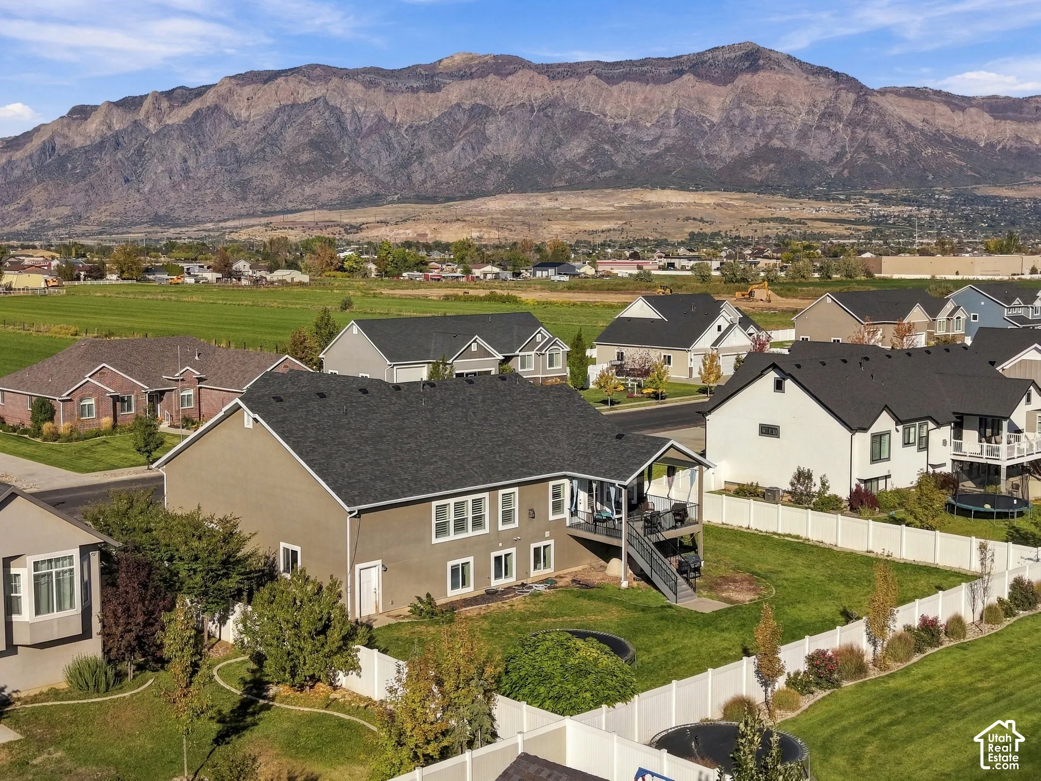 Exterior featuring a mountain backdrop, a rear elevated deck with stairs, a white vinyl privacy fence, and a manicured lawn