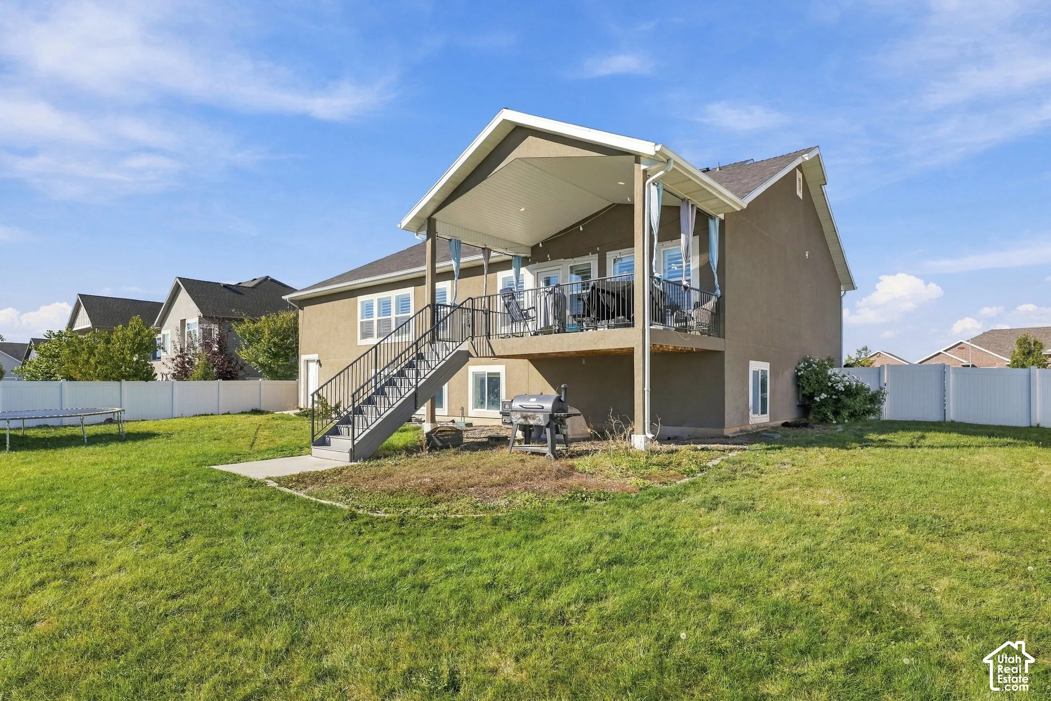Covered rear deck featuring metal railings, staircase, and recessed lighting, overlooking a fenced backyard with a concrete patio