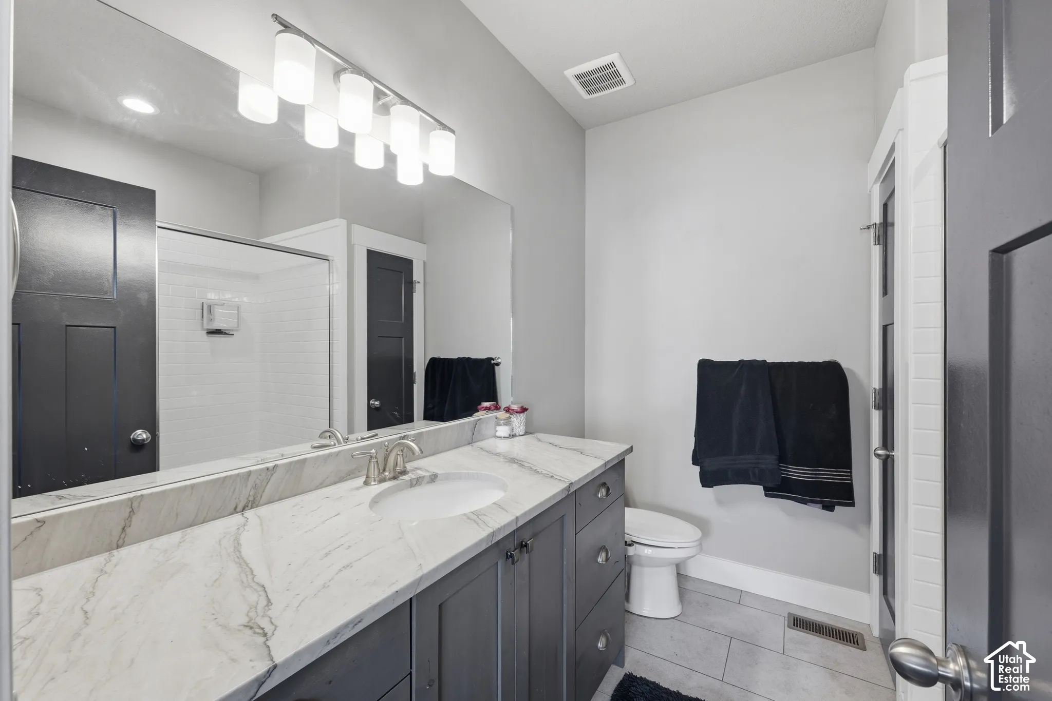 Bathroom featuring a dark-finish vanity with stone-surfaced countertop, under-mount sink, full-width mirror, and tile flooring