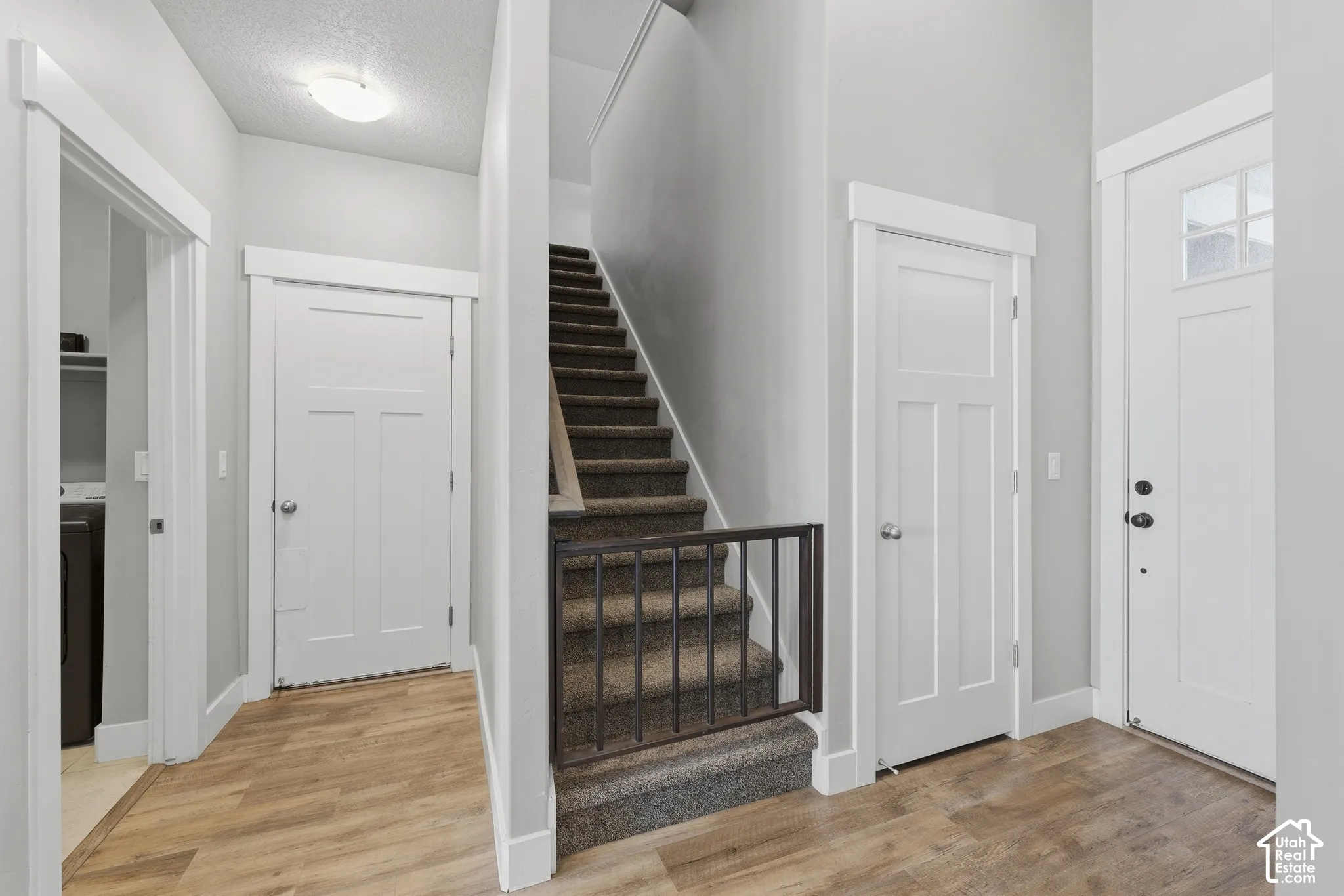 Entryway featuring wood-finish flooring, white shaker-style interior doors, clean-lined trim work, and carpeted staircase