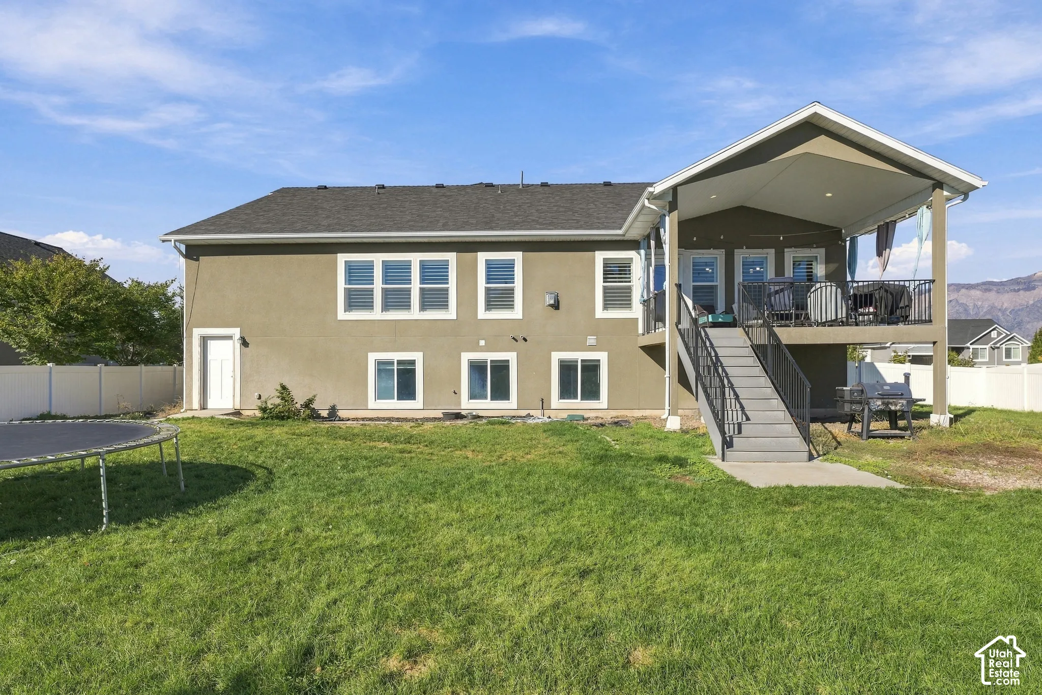 Stucco exterior featuring a covered elevated deck with recessed lighting, metal railings, and a staircase providing access to the fenced backyard