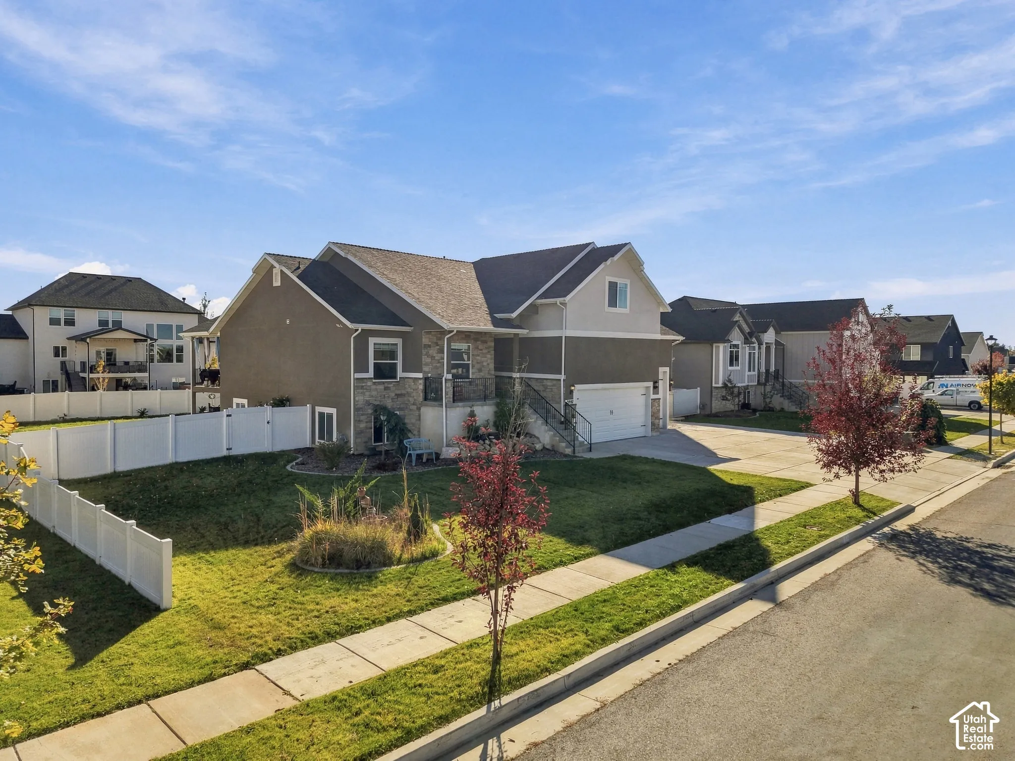 Two-story residence featuring a mixed stucco and stone veneer exterior, an attached two-car garage, and a fenced side yard with a concrete driveway