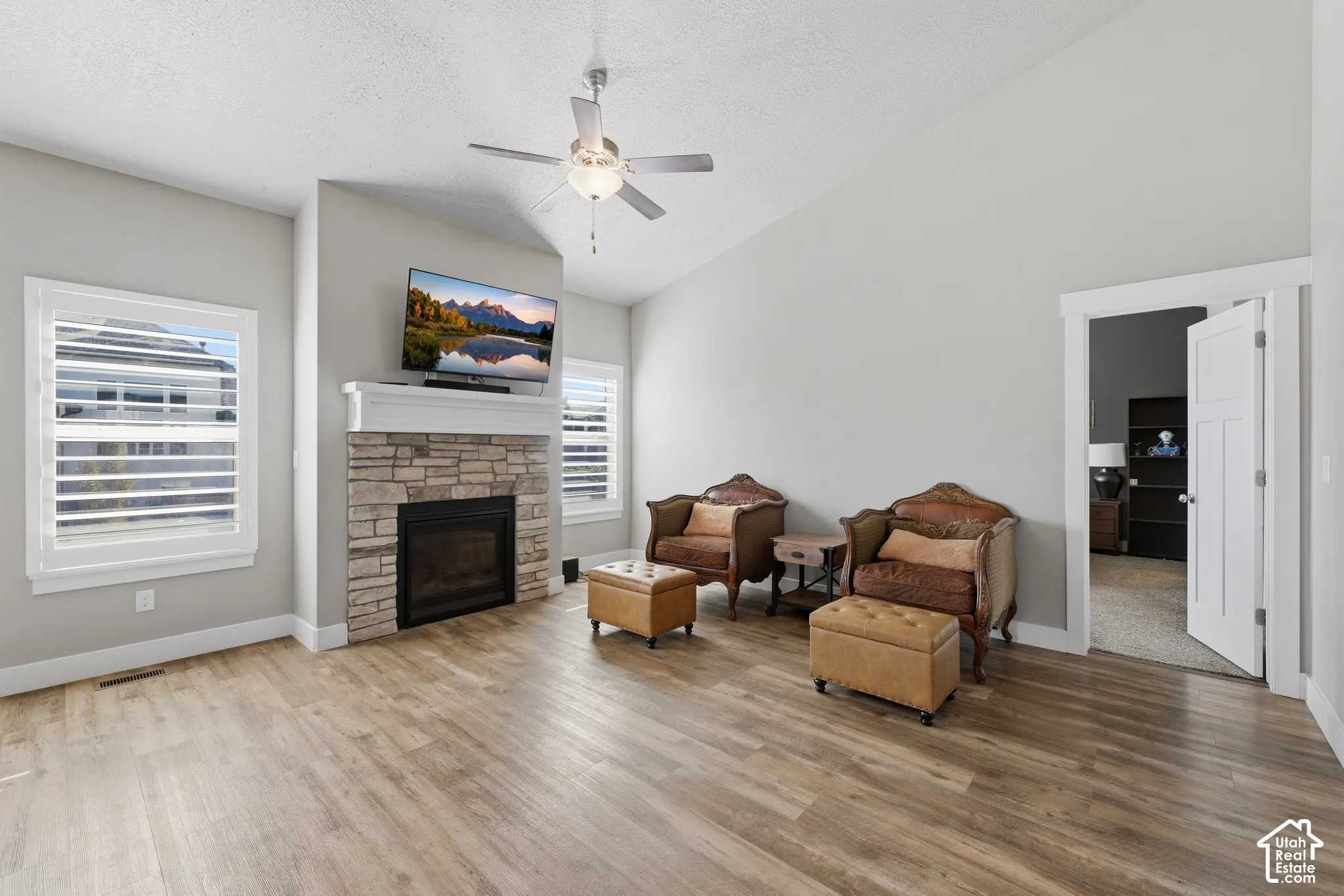 Vaulted ceilings, wood-finish flooring, stone-surround fireplace with a classic mantel, and shuttered windows