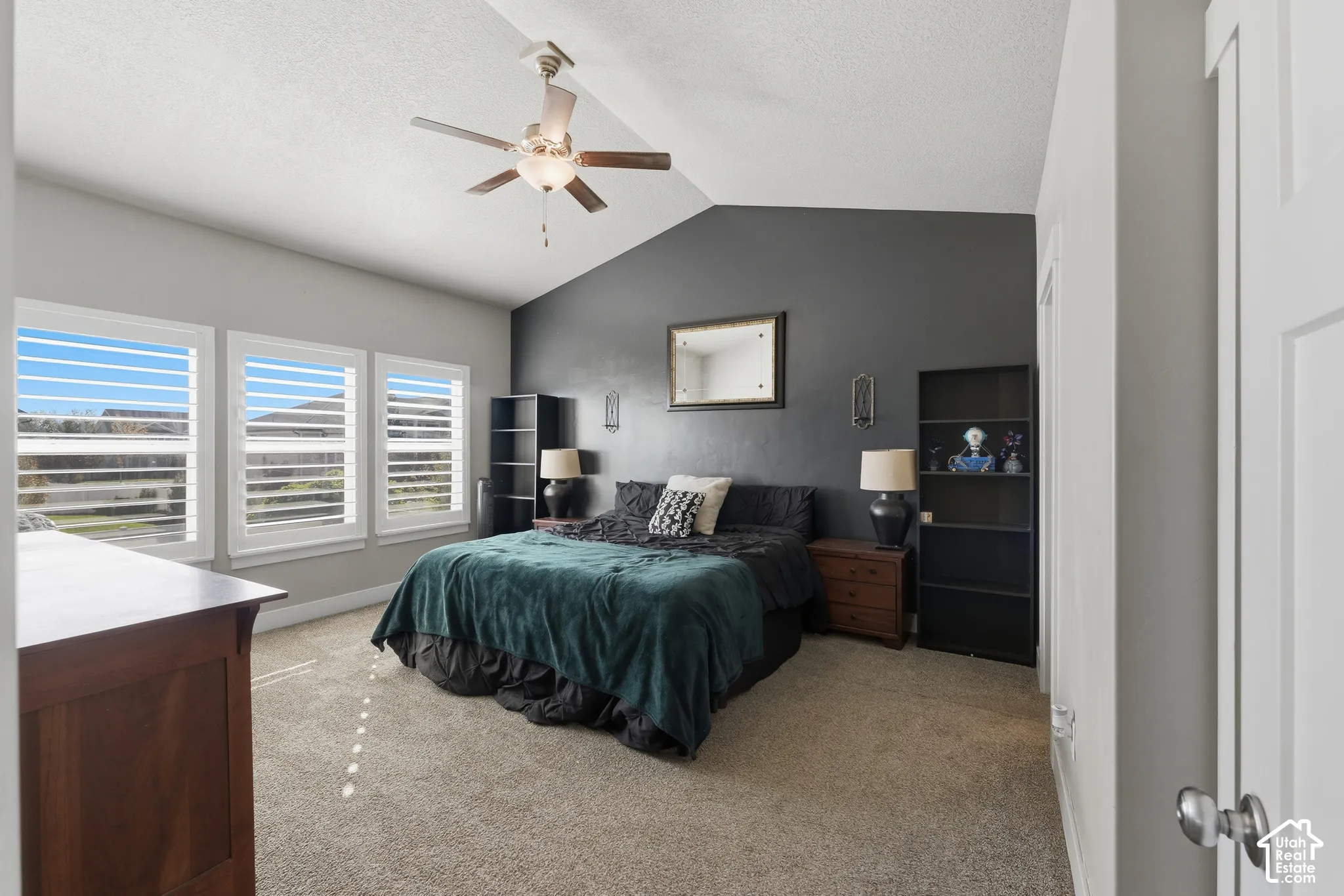Vaulted ceilings, dark-toned accent wall, neutral carpeting, and plantation shutters