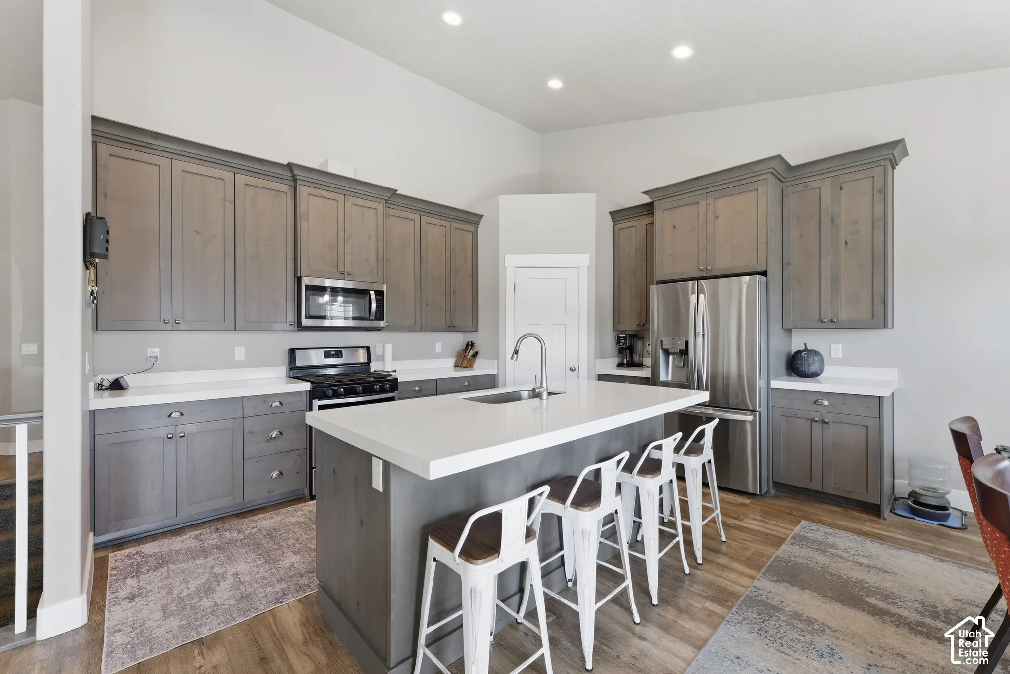 Kitchen featuring gray-toned cabinetry, a central island with a solid-surface countertop, stainless steel appliances, recessed ceiling lighting, and wood-finish flooring