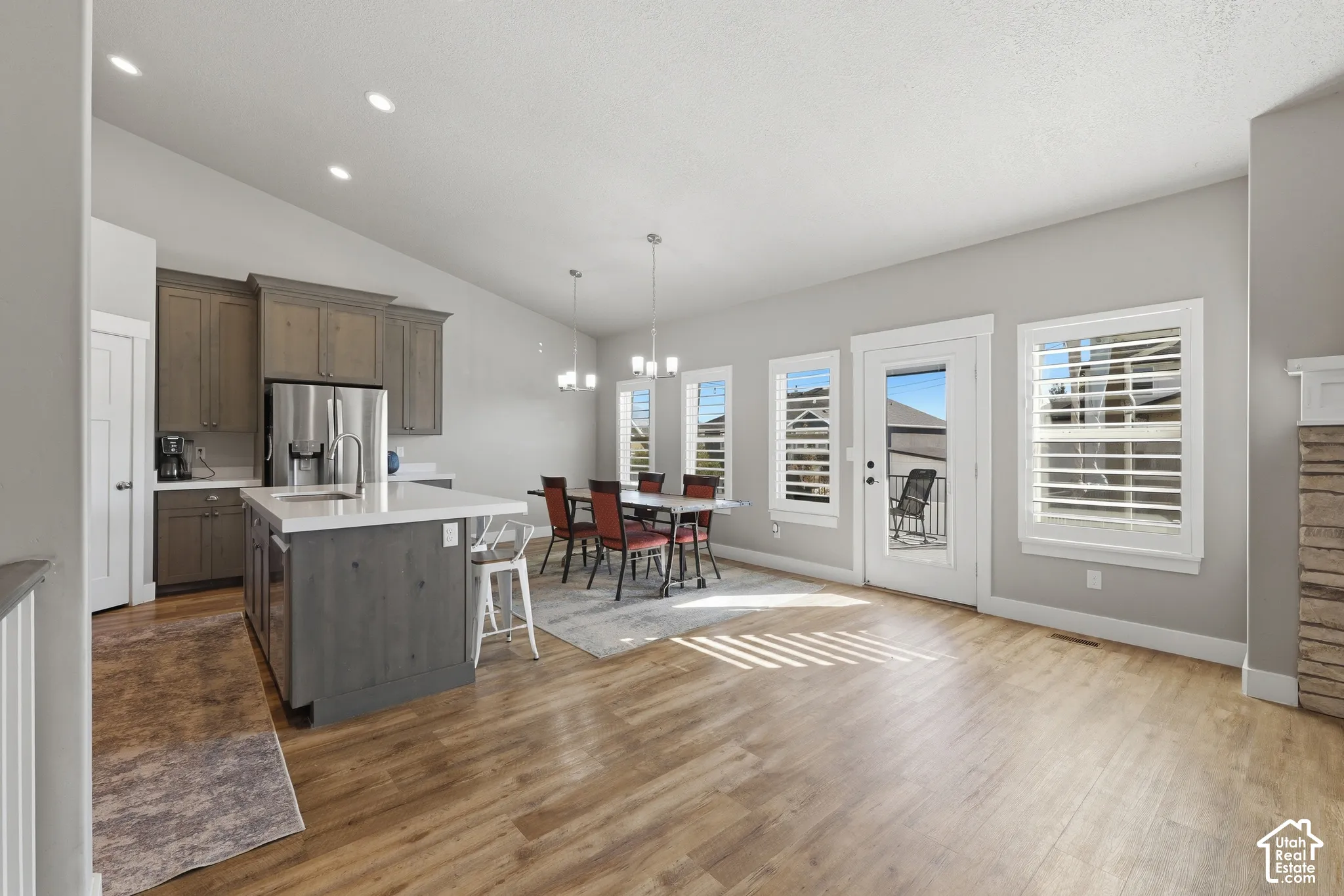 Open-concept kitchen featuring stained cabinetry, a central island with a solid-surface countertop, wood-finish flooring, vaulted ceilings, and windows with interior shutters
