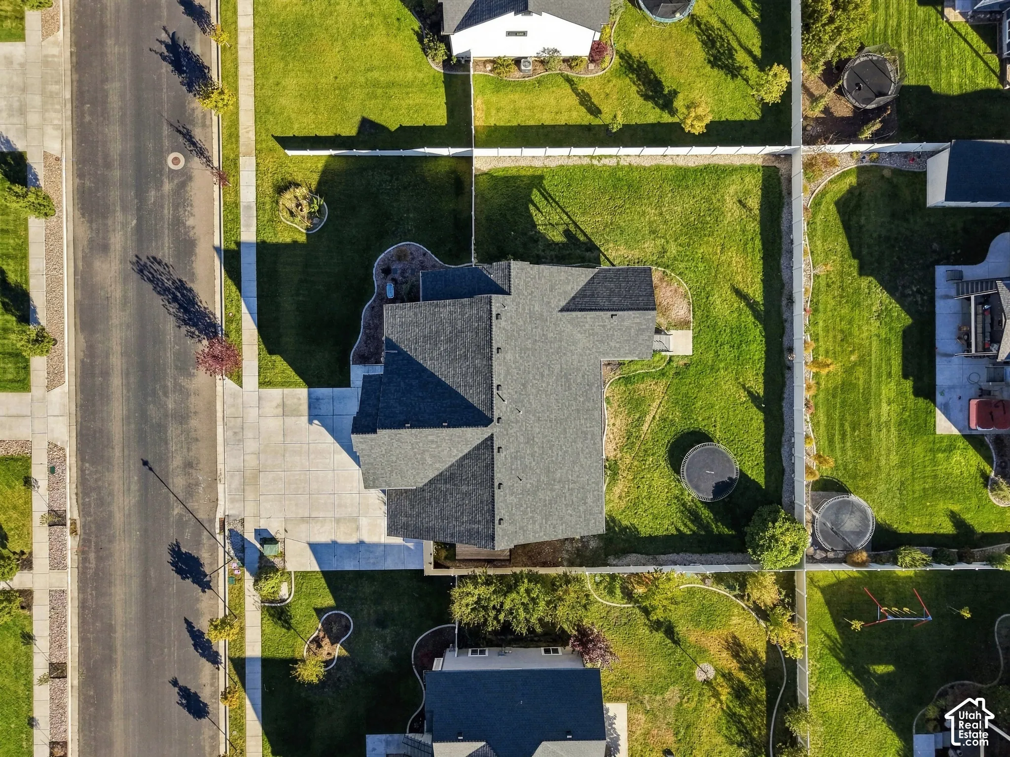 Aerial perspective of a corner lot property featuring a multi-gabled asphalt shingle roof, concrete driveway, and a fully fenced perimeter enclosing a landscaped rear yard