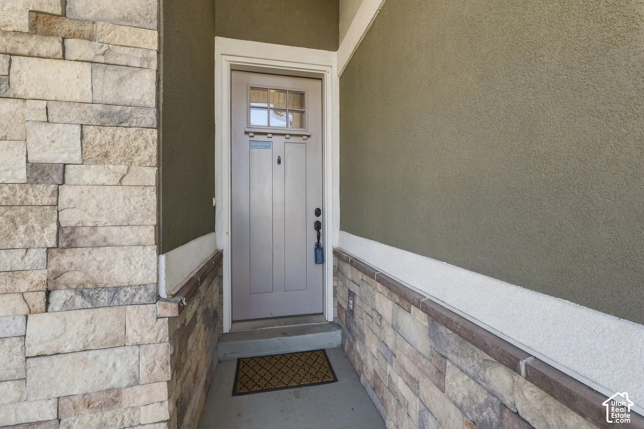 Entryway featuring multi-textured exterior stone veneer, smooth stucco siding, and a solid-core front door with an integrated glass transom window