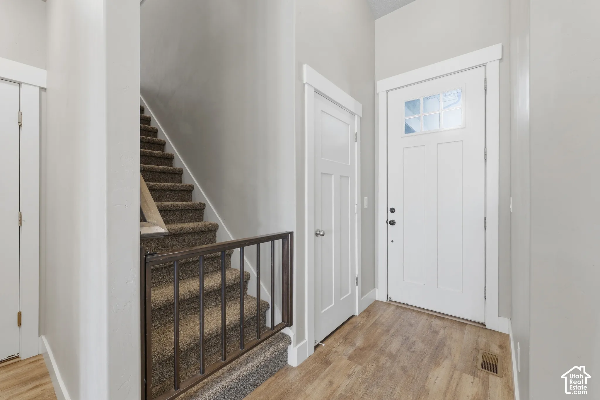 Entryway featuring a white door with a glass transom, wood-finish flooring, and a carpeted staircase with a built-in metal gate