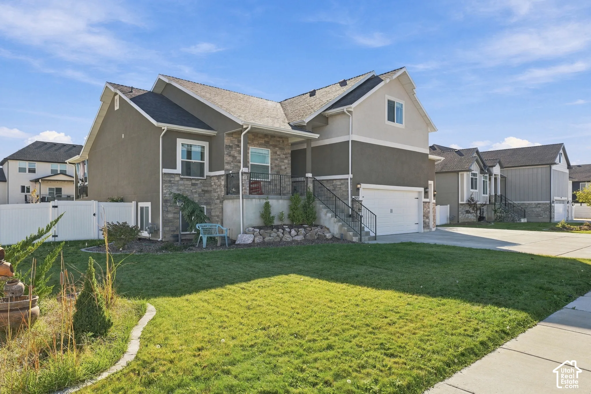 Two-story residence featuring a stone and stucco facade, an attached garage, a concrete driveway, and a raised entry staircase with metal railings