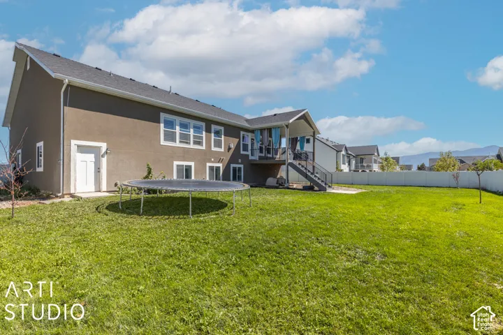 Expansive green lawn, covered deck, white perimeter fencing, and a lower-level access door