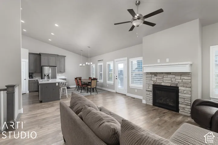 Vaulted ceilings, wood-finish flooring, stone fireplace, kitchen island with seating, and a dining area