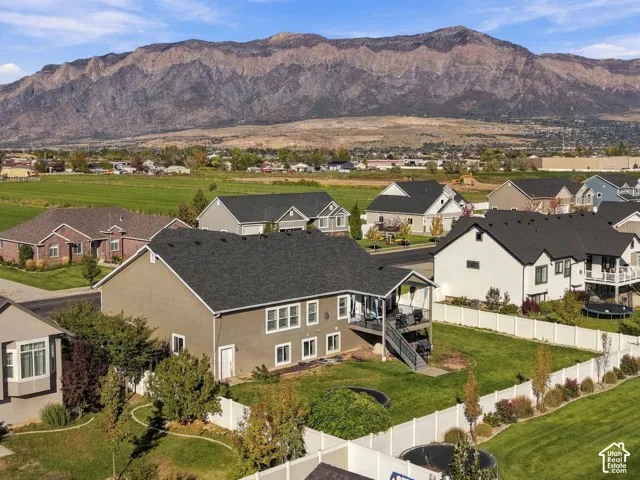 Exterior featuring a mountain backdrop, a rear elevated deck with stairs, a white vinyl privacy fence, and a manicured lawn