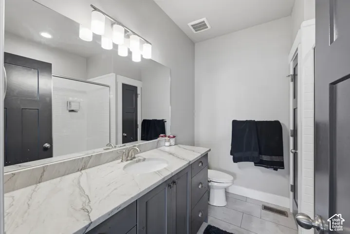 Bathroom featuring a dark-finish vanity with stone-surfaced countertop, under-mount sink, full-width mirror, and tile flooring