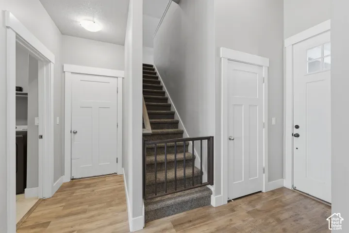 Entryway featuring wood-finish flooring, white shaker-style interior doors, clean-lined trim work, and carpeted staircase