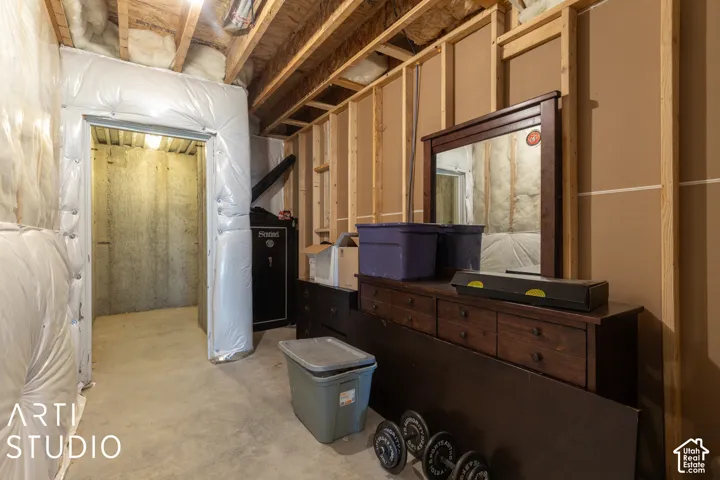 Unfinished basement space with exposed wooden joists and framing, concrete flooring, and a dedicated storage area with concrete walls