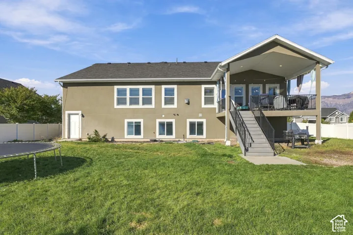 Stucco exterior featuring a covered elevated deck with recessed lighting, metal railings, and a staircase providing access to the fenced backyard