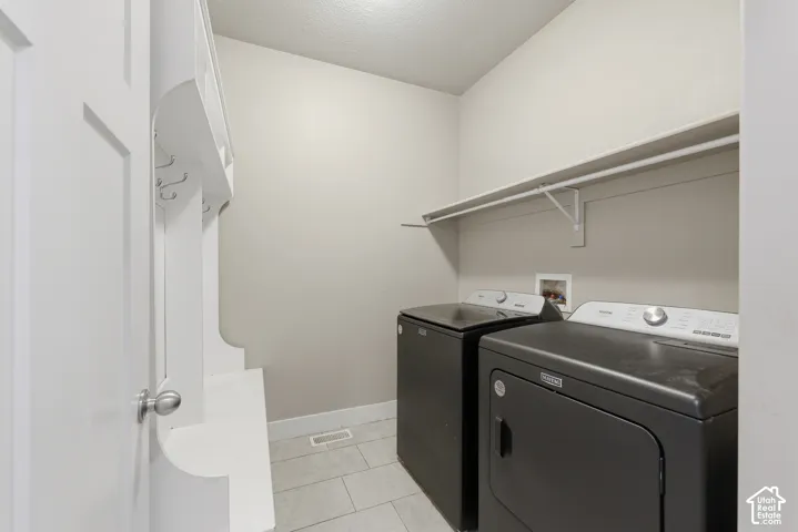 Laundry space featuring tile flooring, white built-in cabinetry with integrated hooks, and an overhead storage shelf