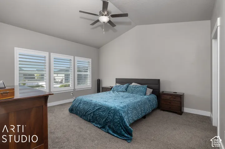 Vaulted ceiling with a ceiling fan, three windows with plantation shutters, light gray wall paint, and gray carpet flooring