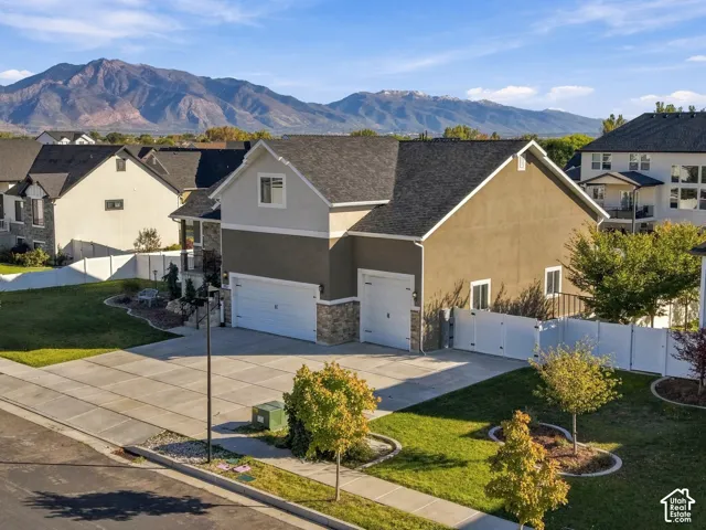 Exterior featuring a multi-car garage, stone veneer base, asphalt shingle roof, white vinyl privacy fencing, and mountain scenery