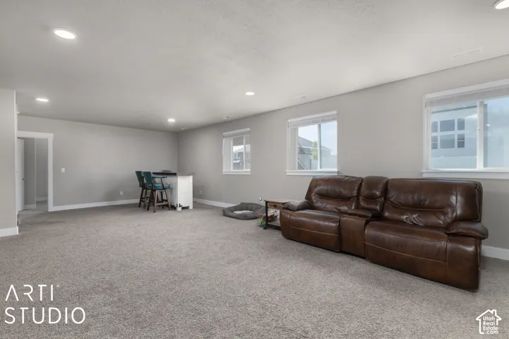 Recessed lighting illuminates a spacious room featuring light gray walls, gray carpeting, and multiple windows