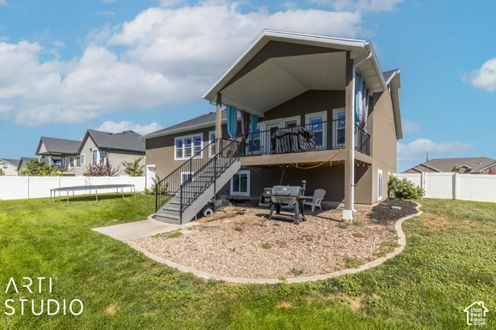 Stucco exterior featuring a covered deck, stairs with black metal railings, and a lower-level concrete patio