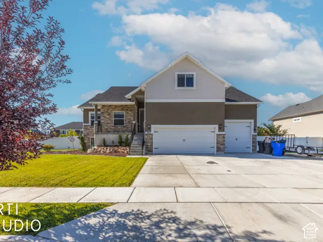 Multi-tone exterior with stone accents, featuring a two-car garage, an additional single-car garage, a concrete driveway, and a manicured front lawn