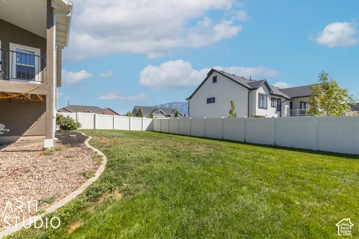 Expansive lawn with a white privacy fence, bordered by a decorative rock bed and concrete curbing