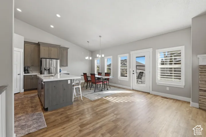 Open-concept kitchen featuring stained cabinetry, a central island with a solid-surface countertop, wood-finish flooring, vaulted ceilings, and windows with interior shutters