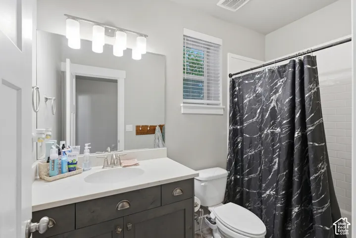 Bathroom featuring a charcoal-toned vanity, white countertop with an integrated oval sink, four-light vanity fixture, and a tile-surround shower
