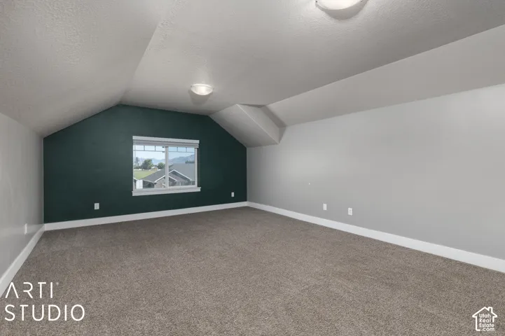 Spacious room featuring sloped ceilings, plush carpeting, a single window, and a contrasting accent wall