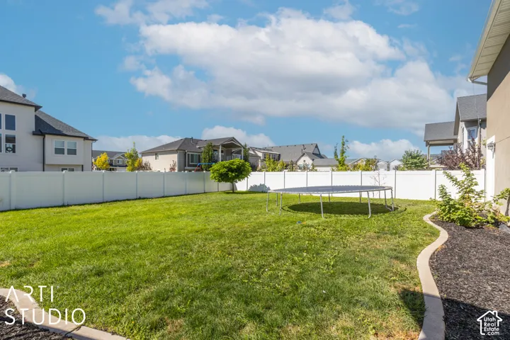 Expansive backyard featuring a manicured lawn, white privacy fencing, and a mulched garden bed