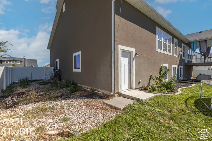 Rear exterior featuring a ground-level entry door, multiple windows, stucco siding, and a partial privacy fence