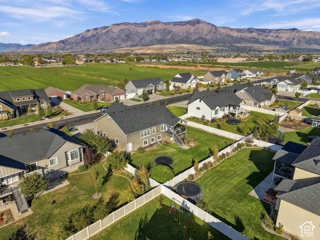 Aerial perspective featuring a multi-story residence with a composite shingle roof, enclosed rear yard, white vinyl perimeter fencing, and prominent mountain backdrop