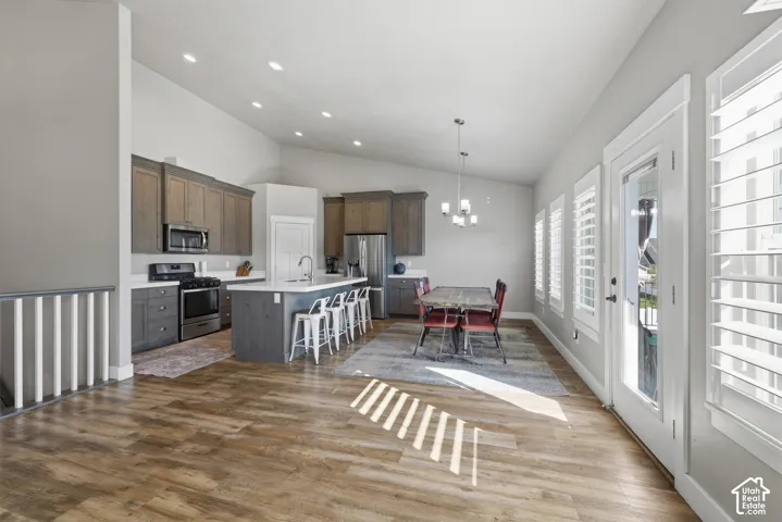 Vaulted ceilings featuring recessed lighting, wood-finish flooring, kitchen island with stone countertop, two-toned cabinetry, and plantation shutters