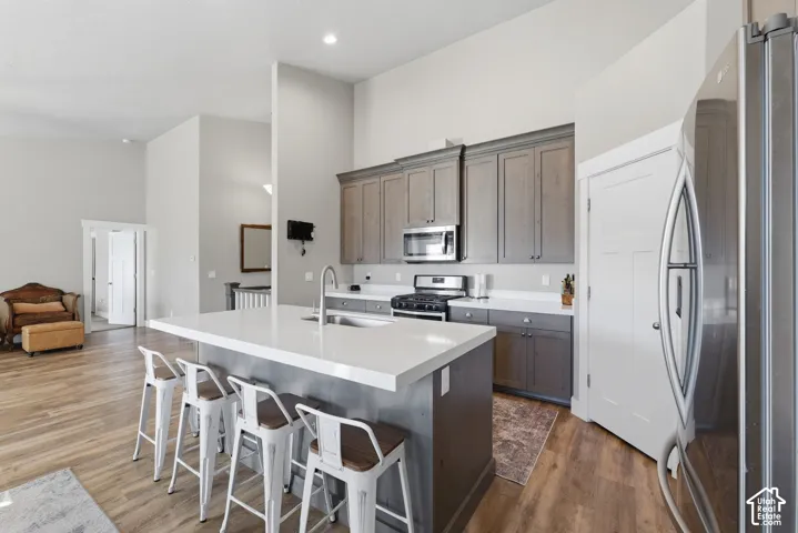 Kitchen featuring an expansive central island with quartz countertops, custom shaker-style cabinetry, stainless steel appliances, and wood-finish flooring under vaulted ceilings