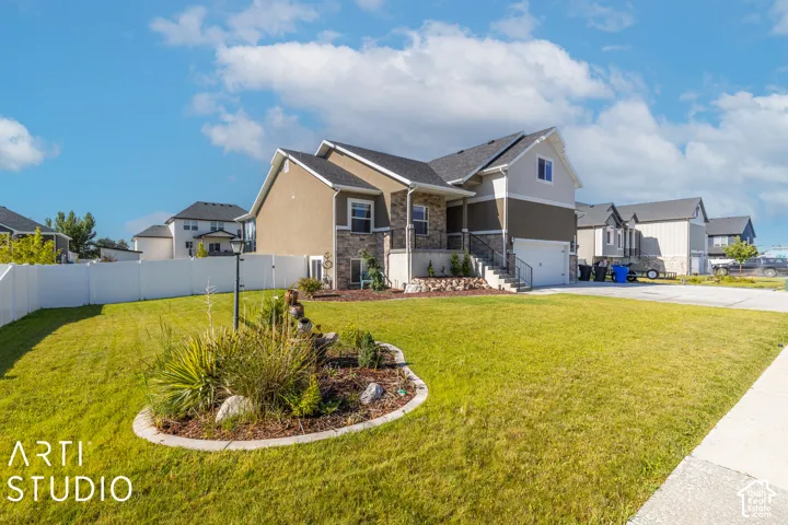 Multi-level residence featuring a stone and stucco exterior, an attached garage, a front porch with railing, a white privacy fence, and a landscaped yard