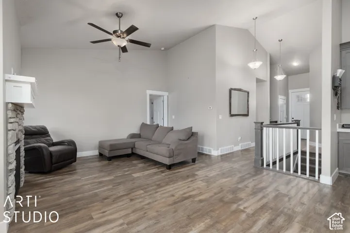 Vaulted ceiling, wood-finish flooring, stone-clad fireplace, ceiling fan, and staircase with white railings