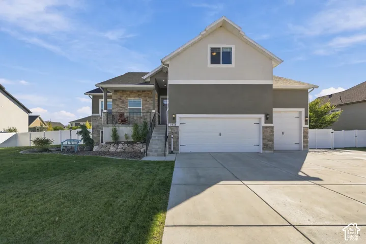 Multi-level exterior featuring a stone facade, dual garage doors, a covered front porch with iron railing, and a concrete driveway