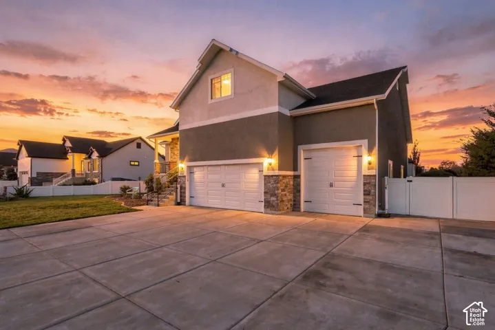 Edited Twilight Photo. Two-story residence featuring a three-car garage, stone veneer siding, concrete driveway, and white vinyl privacy fencing