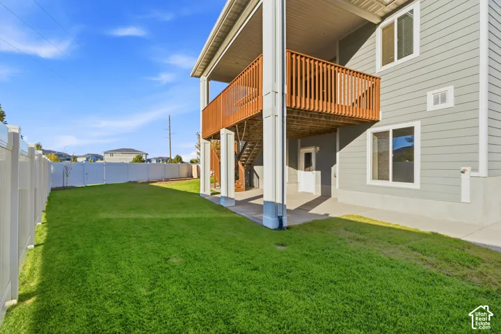 Expansive green lawn, white privacy fencing, upper-level wood-railed balcony, lower-level concrete patio, and light grey siding