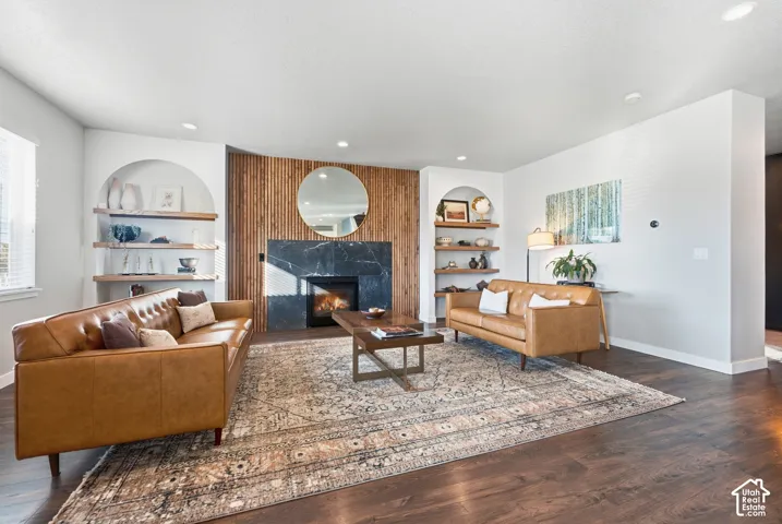 Wood-finish flooring, recessed lighting, built-in shelving, fireplace with dark stone surround, and an accent wall with vertical wood paneling