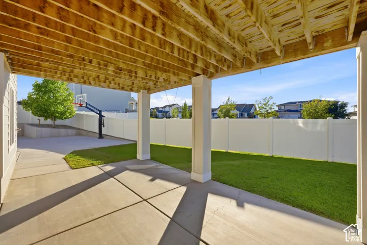 Covered patio with concrete flooring, supported by white columns, featuring a private fenced yard and a level lawn area