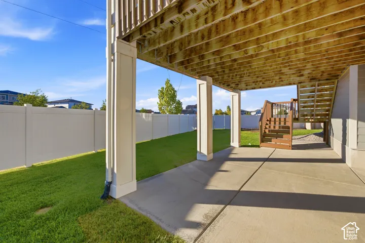 Covered concrete patio, supported by white columns, with a separate wooden staircase to the upper level
