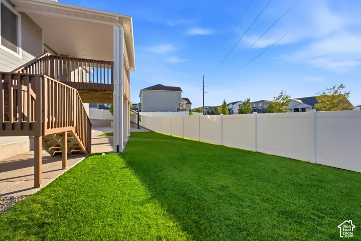 Private backyard with expansive green lawn, white privacy fence, and a multi-level wood deck