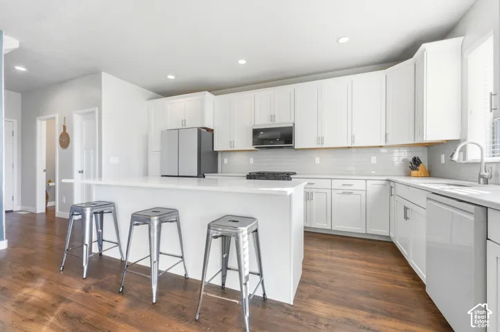 Kitchen featuring white shaker-style cabinetry, a spacious island with a white countertop, new Samsung Bespoke white glass appliances and subway tile backsplash, and wood-finish flooring
