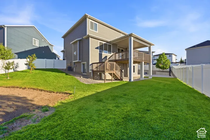 Expansive rear lawn, privacy fencing, covered patio, raised deck, and exterior stairs